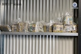 Wads of cash sitting on a shelf mounted on a corrugated iron wall.
