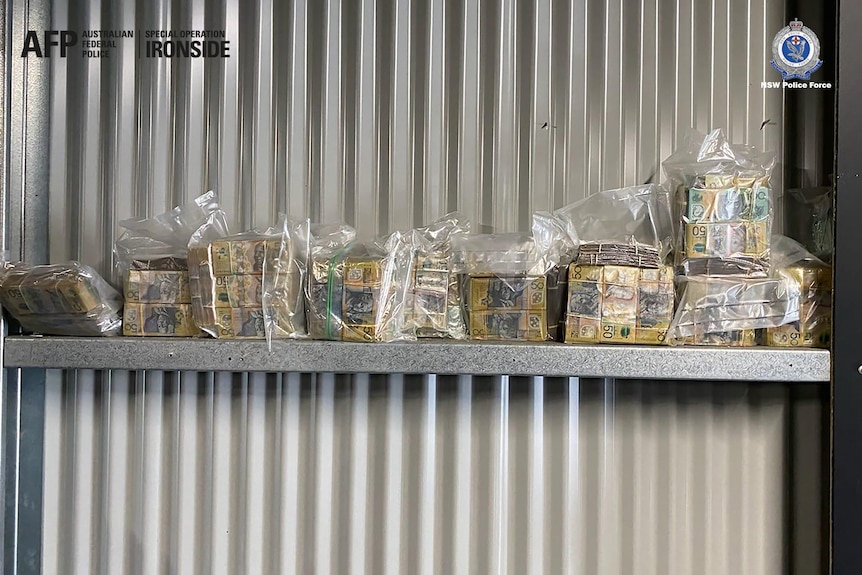 Wads of cash sitting on a shelf mounted on a corrugated iron wall.