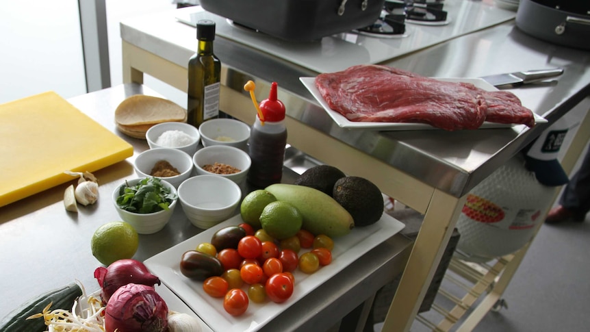 Flank beef fillets, tomatoes, onions, beanshoot, limes, coriander and olive oil sit on cooking bench.
