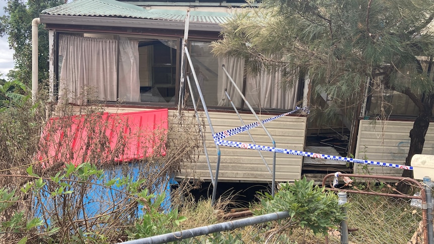 White weatherboard house blocked off by blue and white tape.