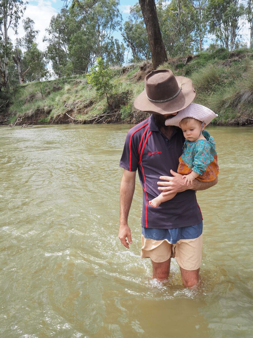 Medium shot of a man standing in a creek holding a baby.