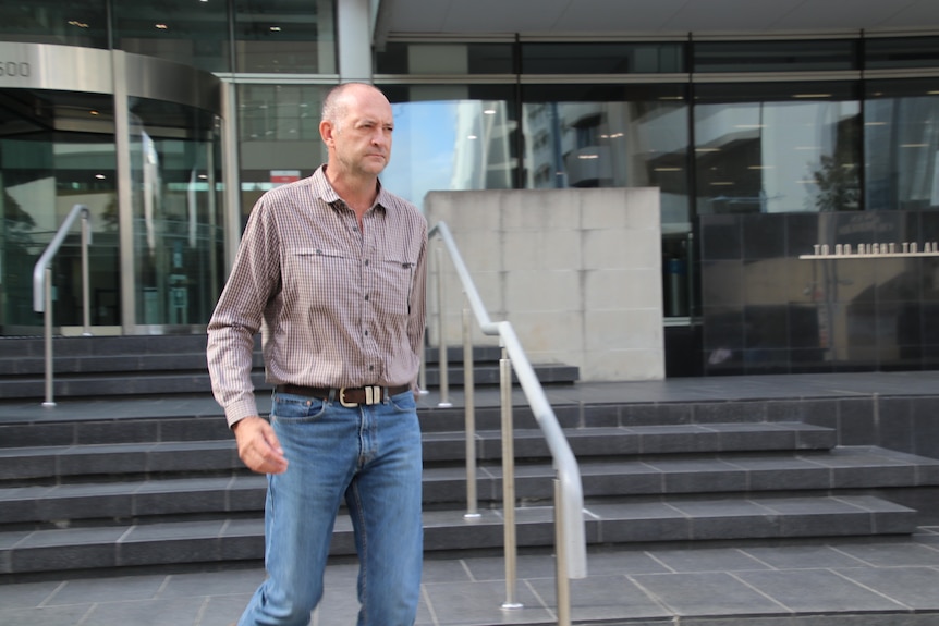 A photo of a man wearing a mushroom-coloured shirt and jeans.