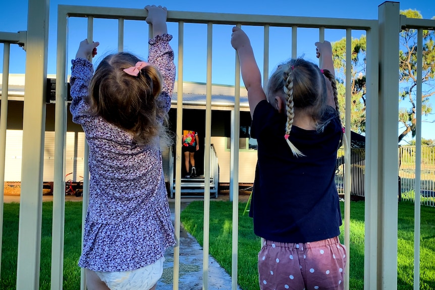 Two little girls hanging on preschool gate.