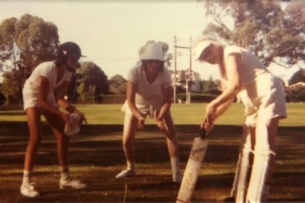 Three women in cricket attire play cricket.