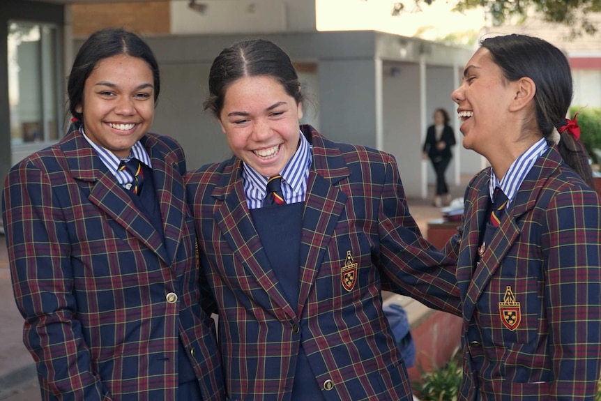 Three girls in their school uniform laugh and smile at each other