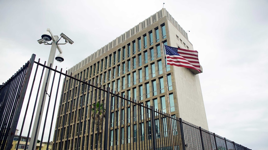 An American flag blows in the wind outside the multi-storey US embassy in Cuba, which is surrounded by a black fence.