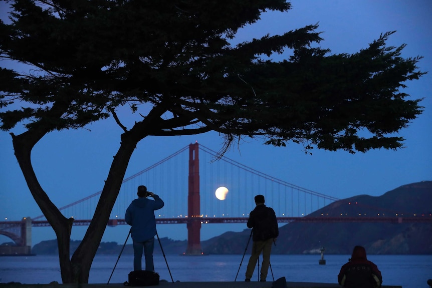 Photographers take a picture of the super blue blood moon setting over the Golden Gate Bridge.