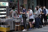 People line up at a newspaper stall in a city strewet.