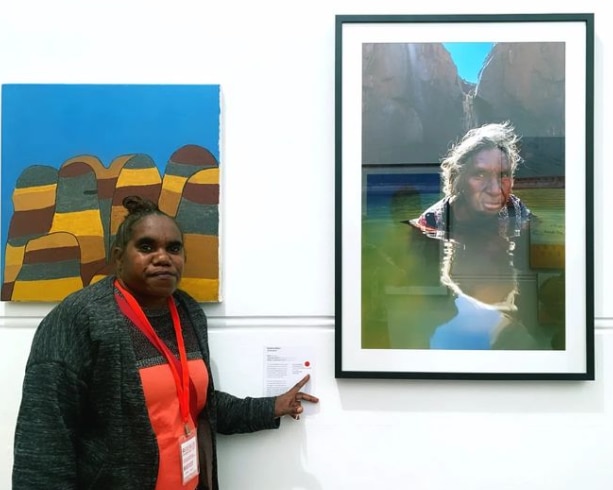 A woman pointing at a red dot a plaque next to a framed photo.