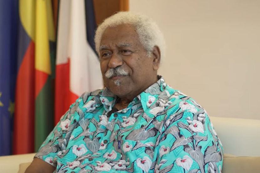 Kanak politician Roch Wamytan with fuzzy white hair sits in an office chair wearing blue floral shirt. 