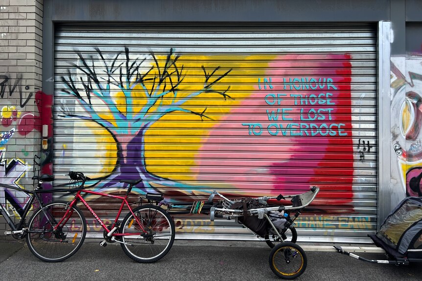 Multi-coloured mural on garage door reads In Honour of Those We Lost to Overdose next to a painting of a tree.