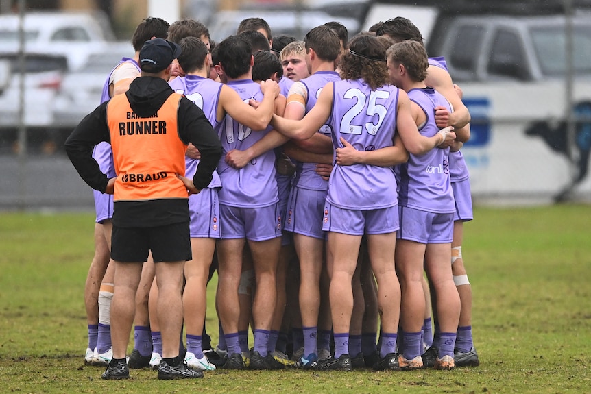 A group of football players wearing purple jumpers huddle together. 