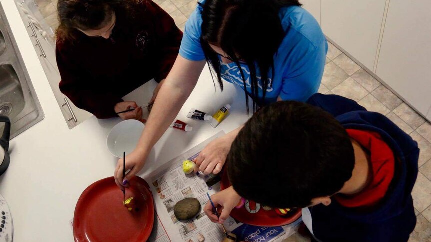 Three children in care in Canberra decorate rocks in a kitchen.
