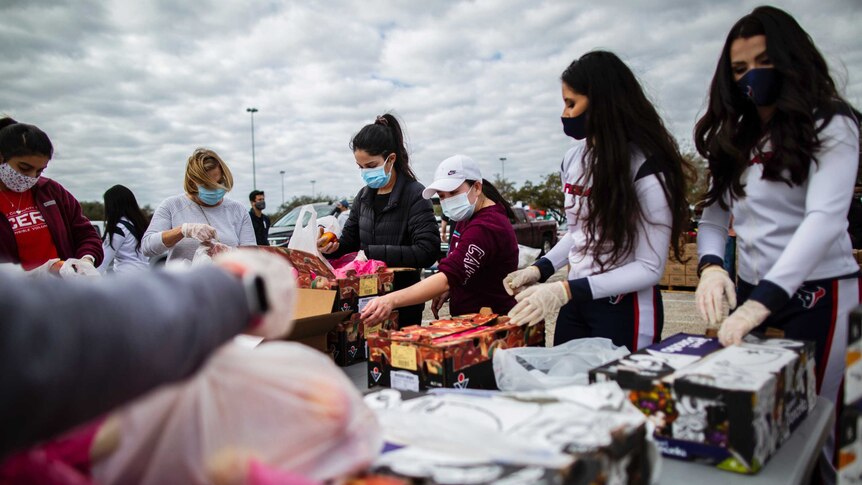 A group of women and young girls wearing face masks pack food