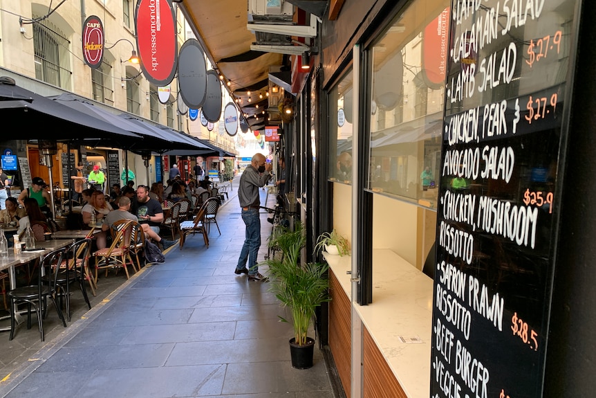 People dine on outdoor tables covered by umbrellas on Melbourne's Degraves Street.