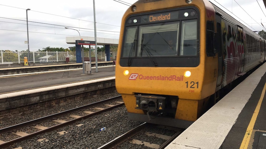 A Queensland Rail passenger train pulls in at a station.