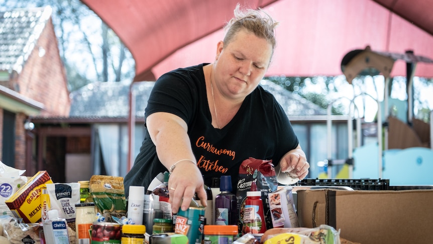 Chandelle Wilson leaning over a table covered in pantry foods like vegemite and sauce, filling bags for Foodbank.