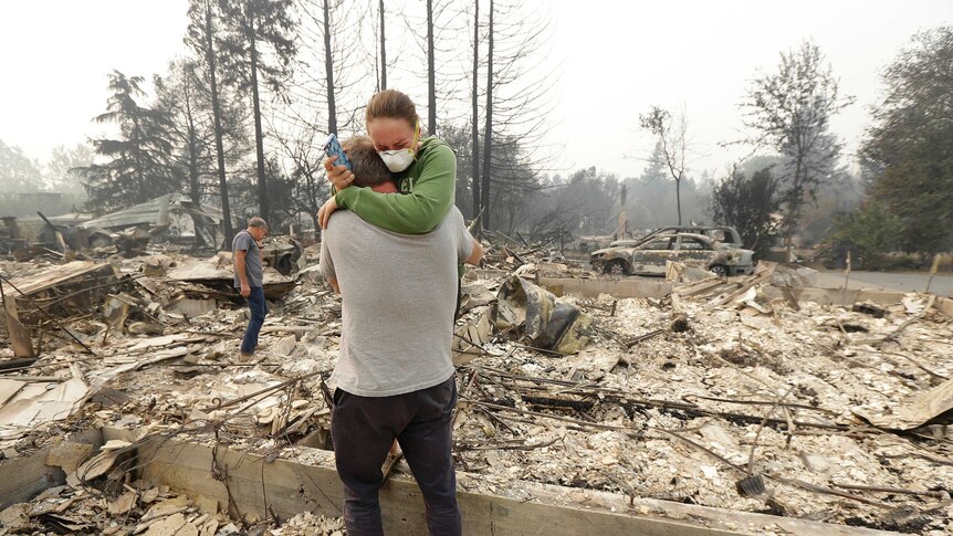 A man hugs his daughter in the ashy ruins of what was once their home.