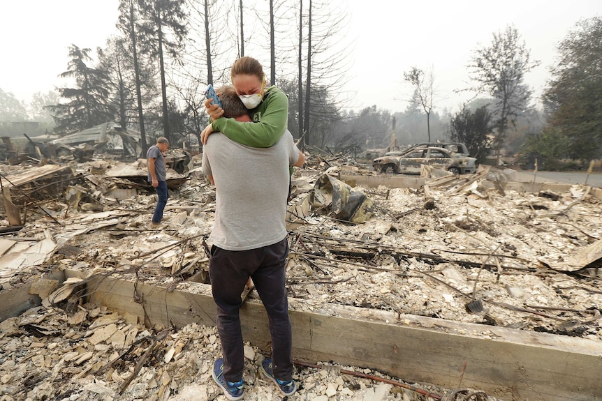 A man hugs his daughter in the ashy ruins of what was once their home.