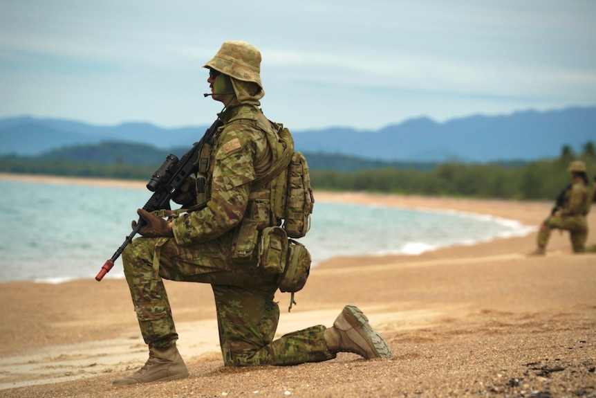 An infantry soldier in combat uniform keeps lookout on a beach in North Queensland.