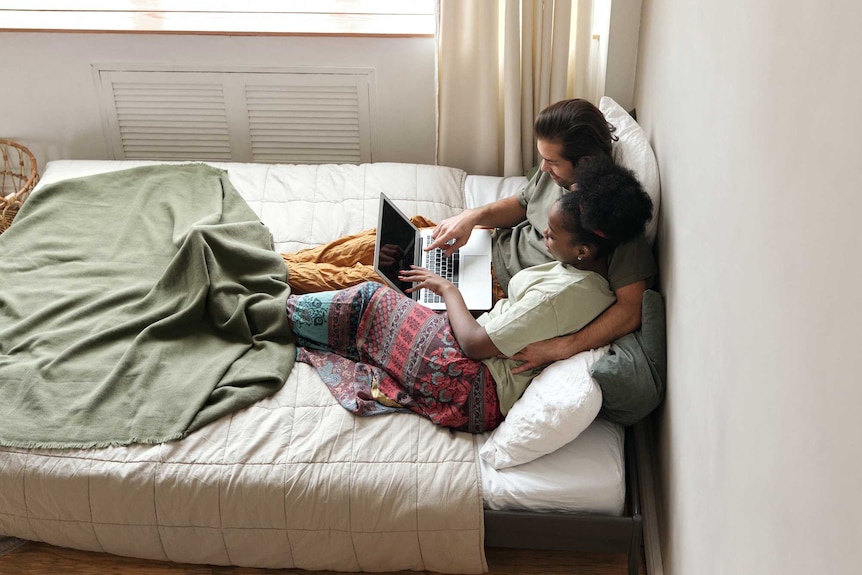 Aerial shot of couple looking at laptop in bed