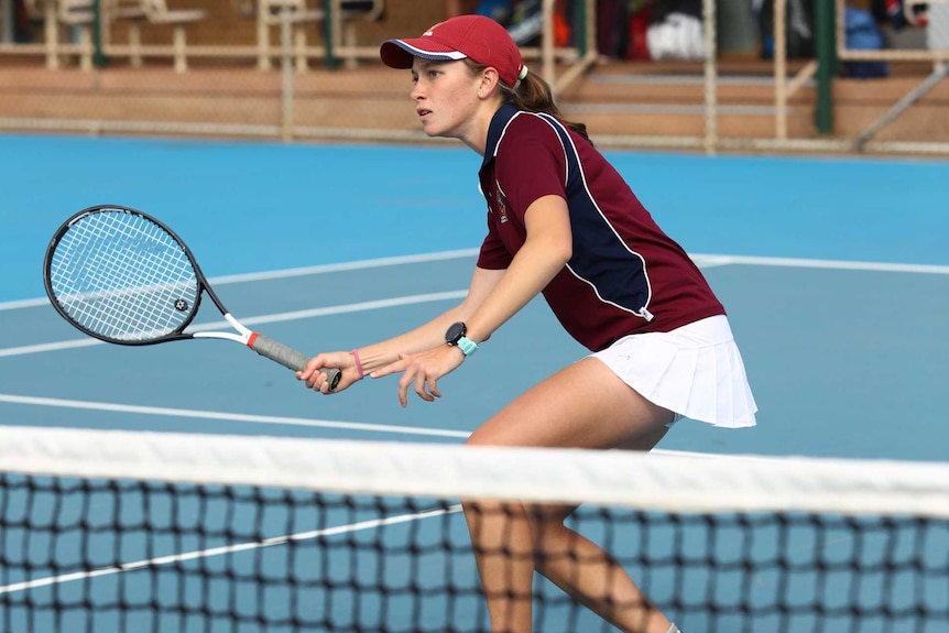 A girl on a tennis court extends a racquet, ready to hit a ball.