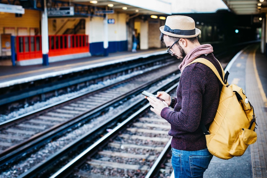 Man standing on a train platform looking at his smartphone.