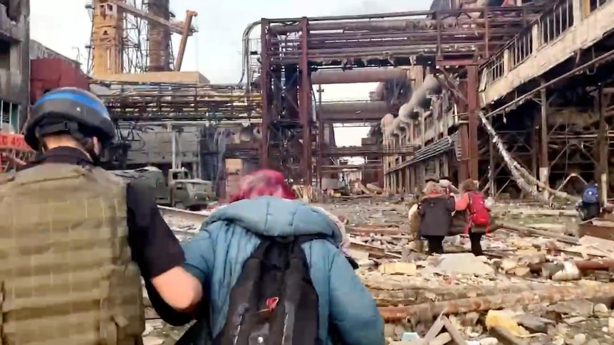 Soldiers help civilians out of a debris ridden steel mill.