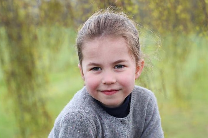 Princess Charlotte sits on a fence smiling