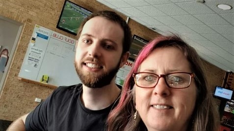 A woman in glasses with a red streak and a man with a beard smile in a pub