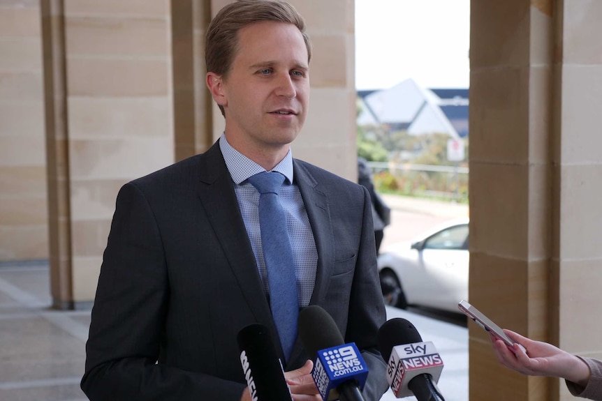  CCI WA chief economist Rick Newnham standing in front of media microphones