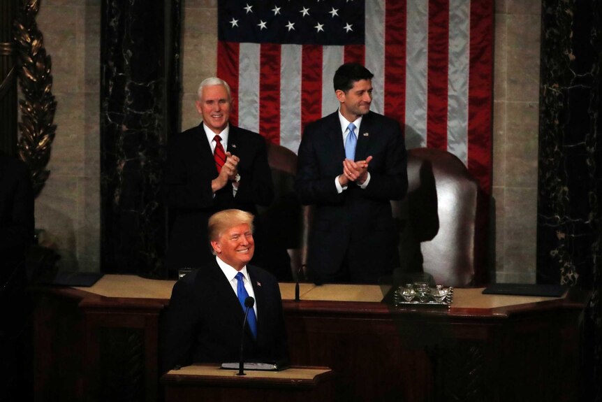 US President stands at a lectern at the US Congress with VP Mike Pence and House Speaker Paul Ryan directly behind him