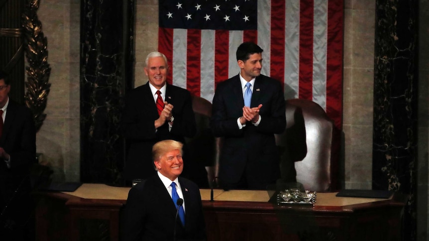 US President stands at a lectern at the US Congress with VP Mike Pence and House Speaker Paul Ryan directly behind him