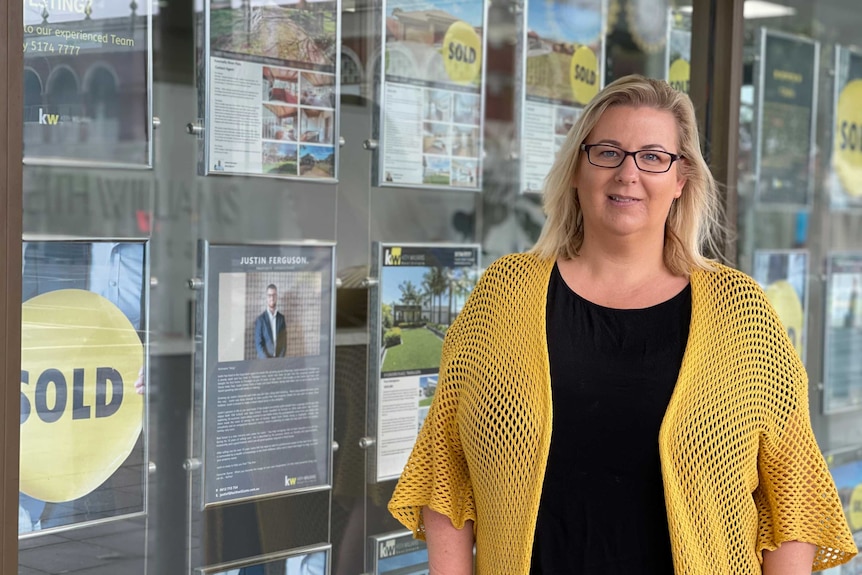 A woman stands in front of a real estate window.