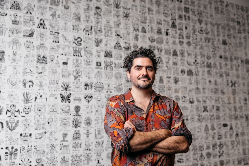 Tom O'Hern stands with his arms folded in front of his Ramsay Art Prize entry, a collection of cartoons tessellated together