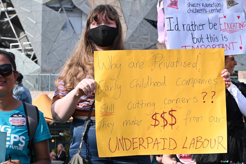 a woman holds a sign that says "early childhood companies... make money from our underpaid labour"