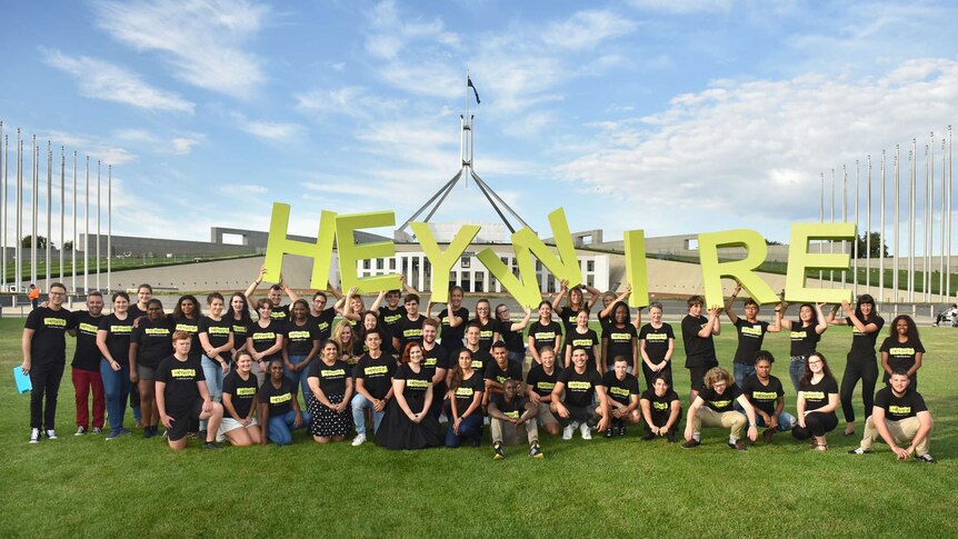 Young people in black t shirts standing outside the federal parliament holding letters spelling heywire