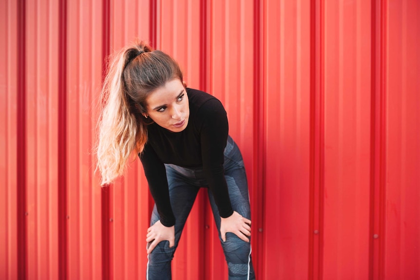 A woman in exercise gear resting by a red wall.