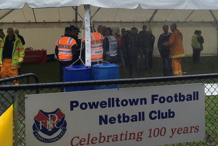 Emergency workers stand under a white tent on an oval during the rain.