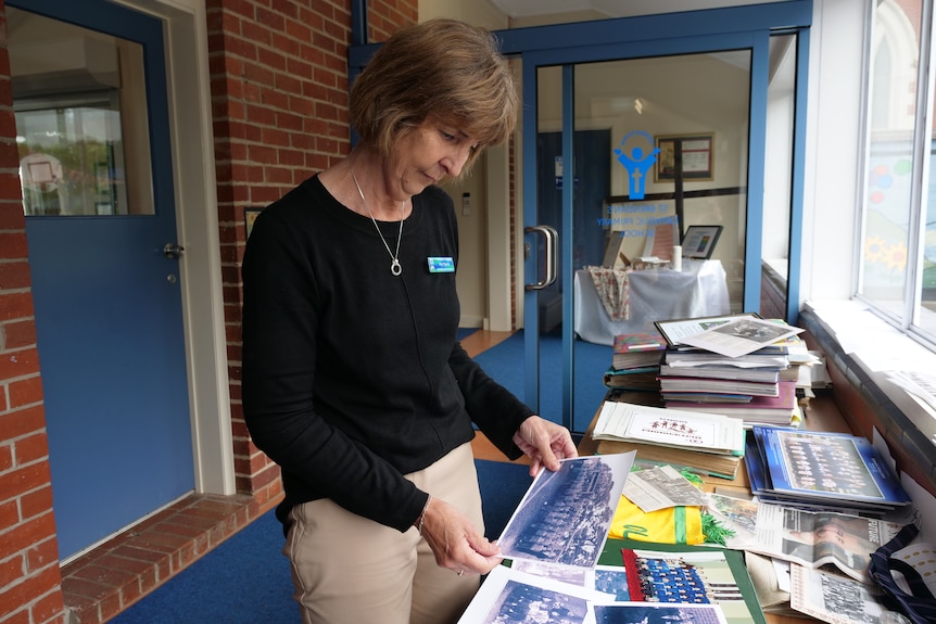 A woman stands in font of a table and looks down at historical school photos.
