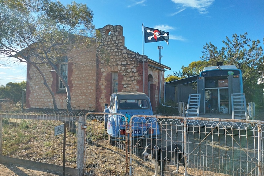 An old stone church building with a car, bus, dog and pirate flag out the front. 
