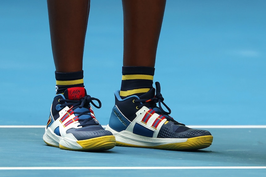 A person wears blue, white, tellow and red shoes on a blue tennis court.
