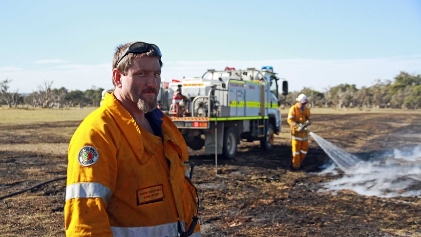 A firefighter looks to the camera, as another extinguishes a private burn in the background.