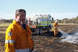 A firefighter looks to the camera, as another extinguishes a private burn in the background.