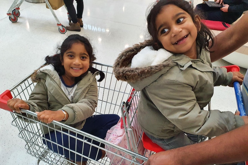 Kopika and Tharnicca sitting in a shopping trolley smiling at the camera. 