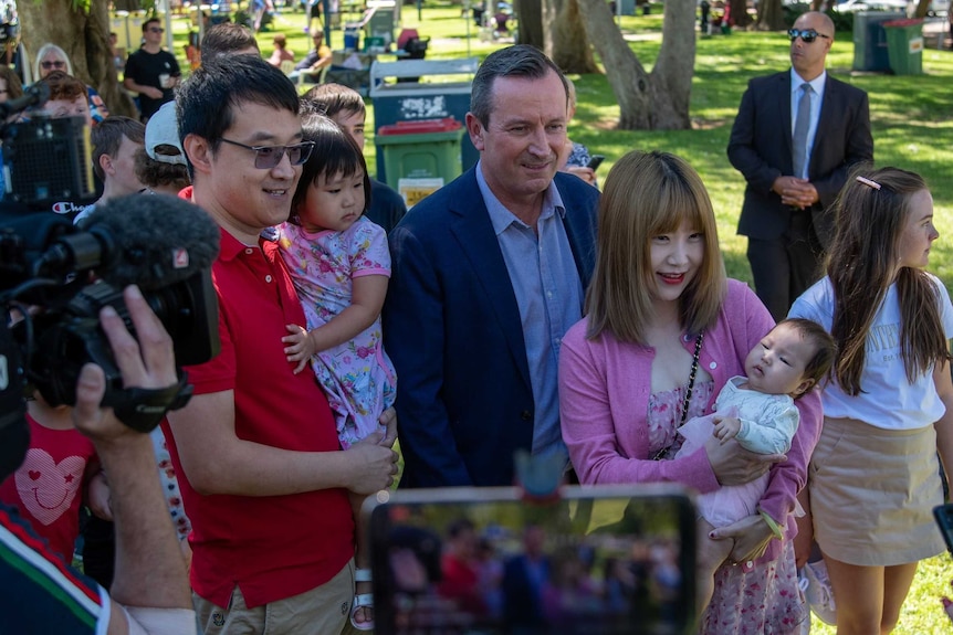 A wide shot of Mark McGowan with a family surrounded by media, security and supporters.