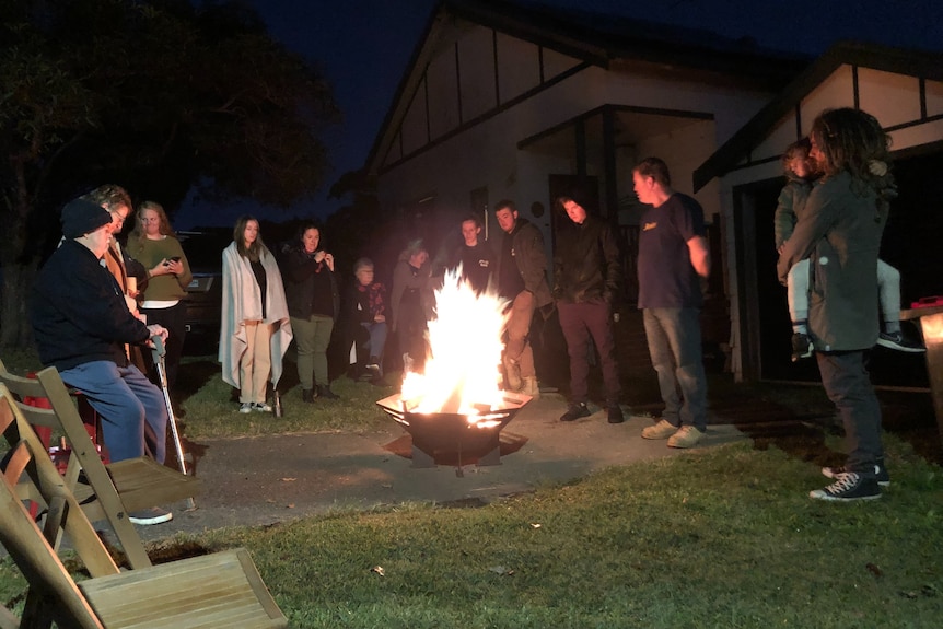 A group of more than 10 people in winter clothes stand around a fire bucket