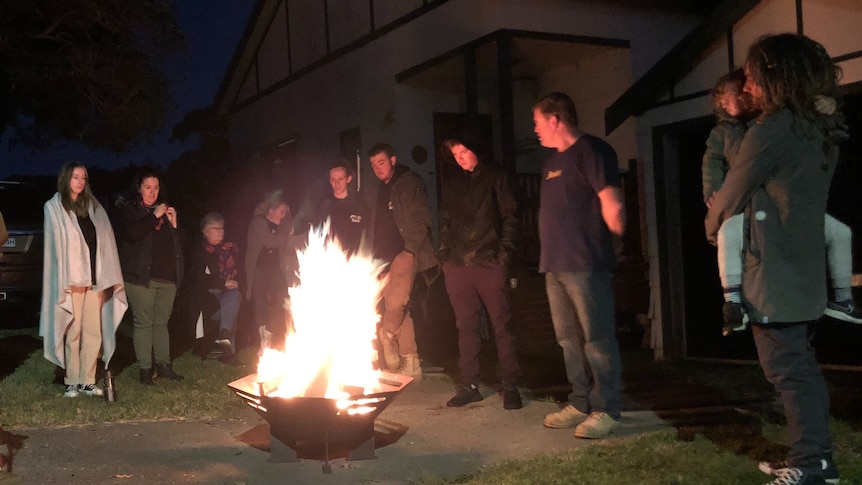 A group of more than 10 people in winter clothes stand around a fire bucket