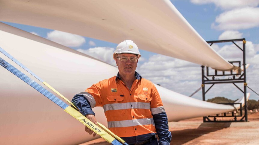 A man wearing high-vis workwear standing next to a blade for a wind turbine.