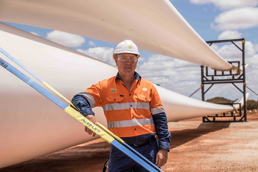 A man wearing high-vis workwear standing next to a blade for a wind turbine.